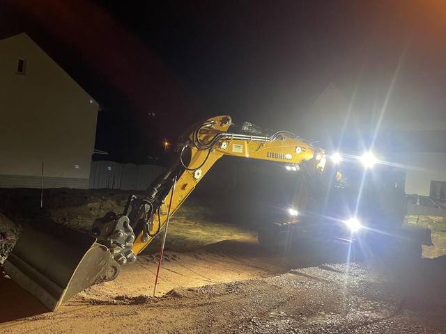 Bagger mit Arbeitsscheinwerfern im Nachteinsatz auf einer Baustelle